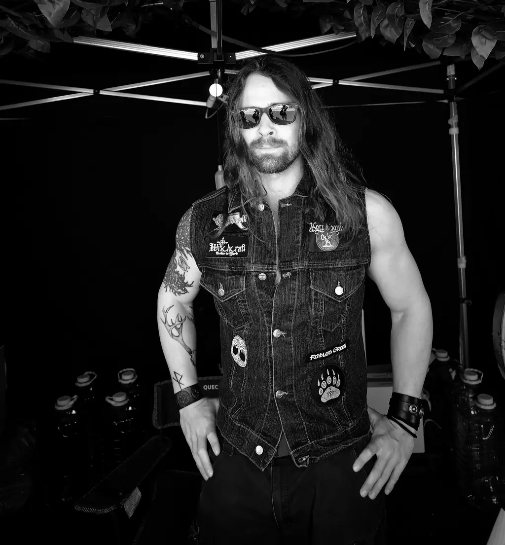A long-haired, tattooed rider in sunglasses and a patched vest