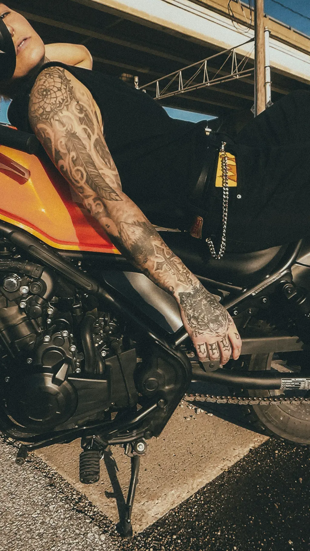 A tattooed arm resting across a motorcycle tank
